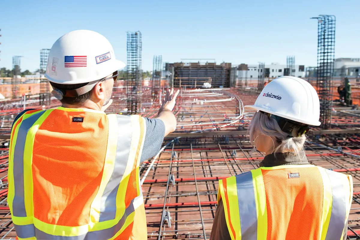 UK civil engineer in a hi-vis jacket and hard hat reviewing construction drawings beside a major infrastructure site