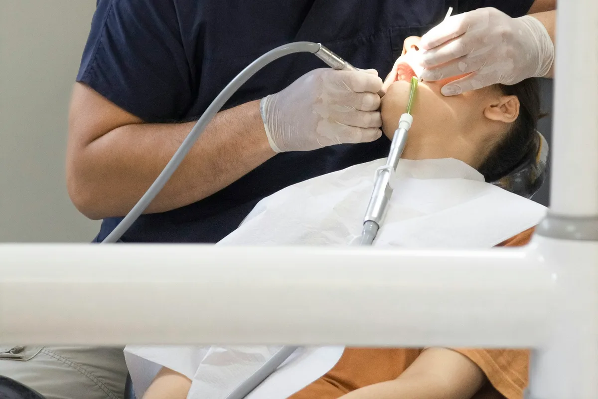 UK dentist in clinical scrubs treating a patient in a modern dental surgery