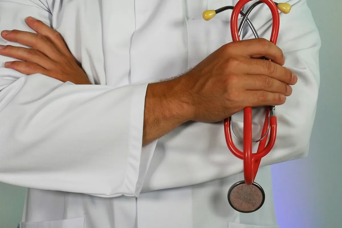 UK doctor in white coat with a stethoscope reviewing a chart in a modern hospital corridor