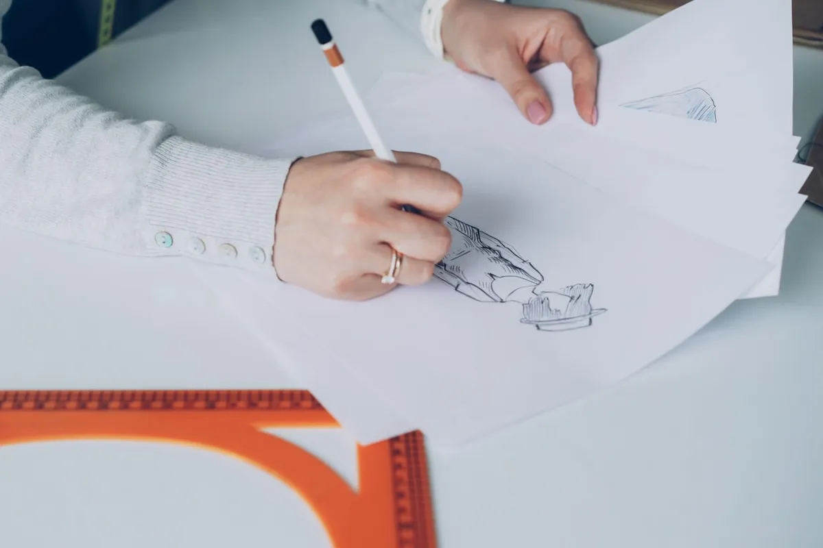 Hands sketching a garment design on paper with a set square in a fashion studio