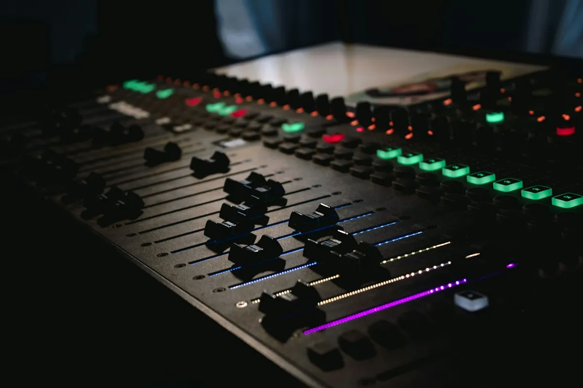 Close-up of an audio mixing console with illuminated coloured faders and controls