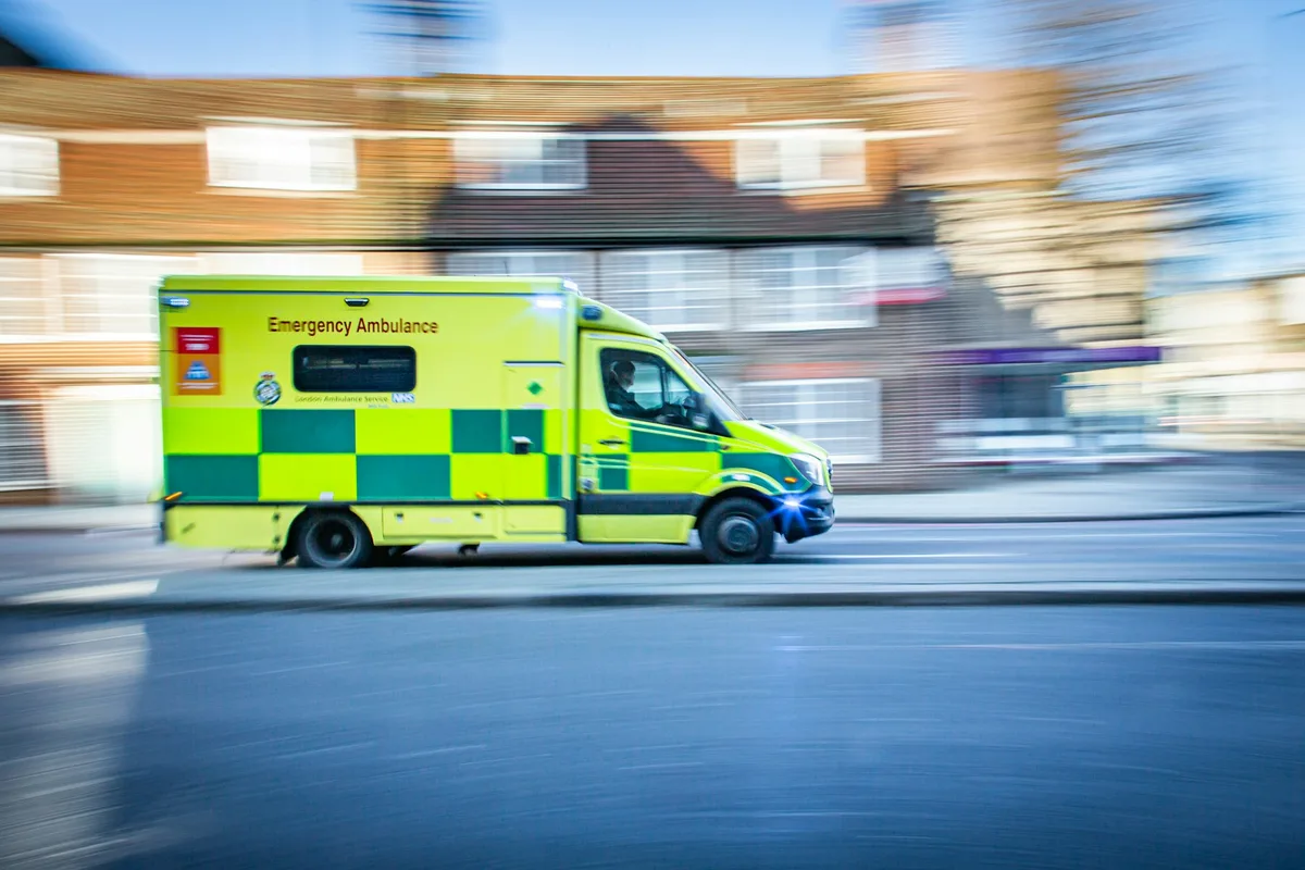 UK paramedic in green uniform attending to a patient beside an ambulance